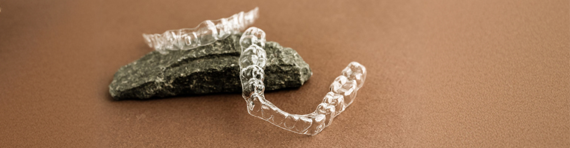 Clear Invisalign aligners displayed on a stone surface.